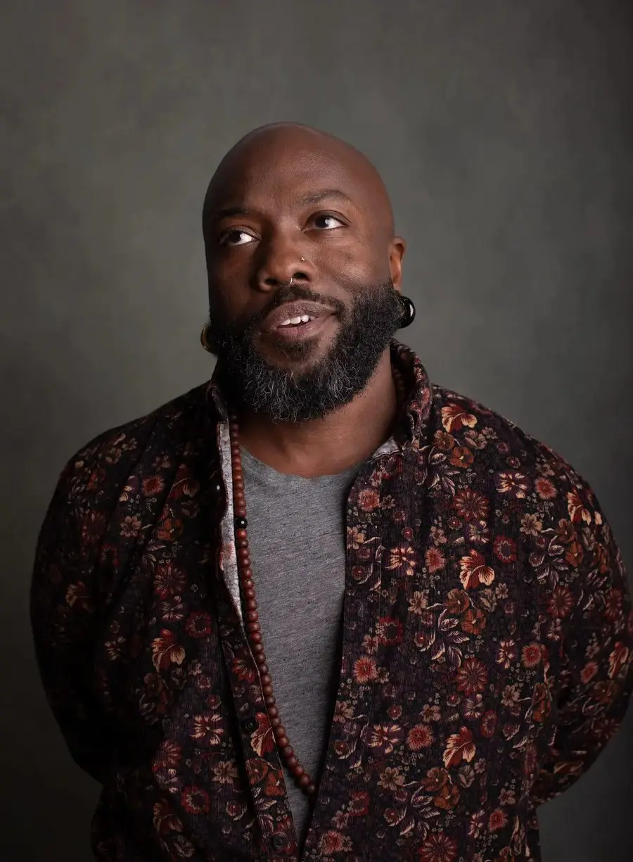 quincéy in a flowered shirt, looking up and to the side, mid-word.