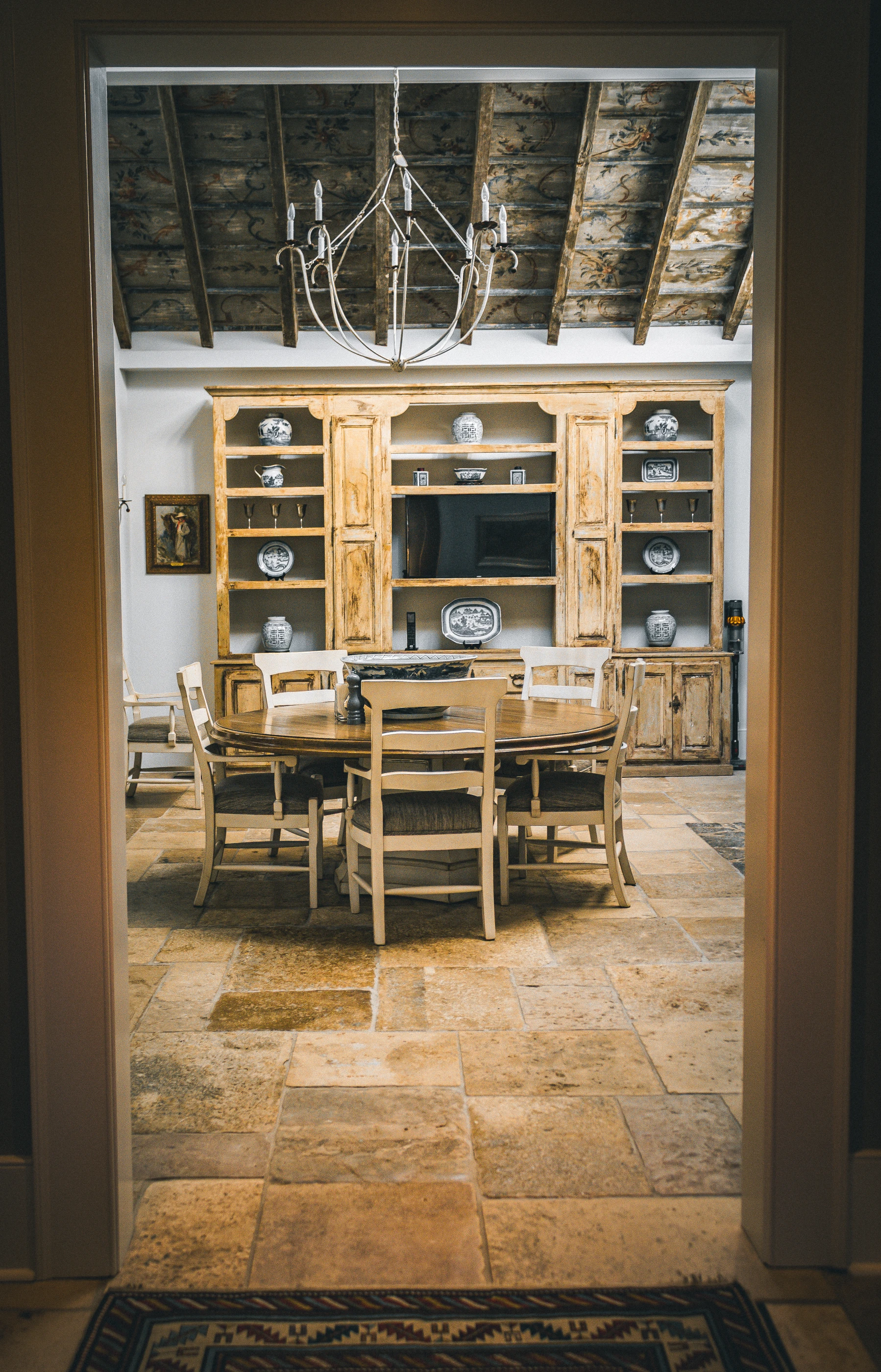 A framed threshold at Reed Farm reveals a dining space with warm timber, antique furniture and patterned textiles.