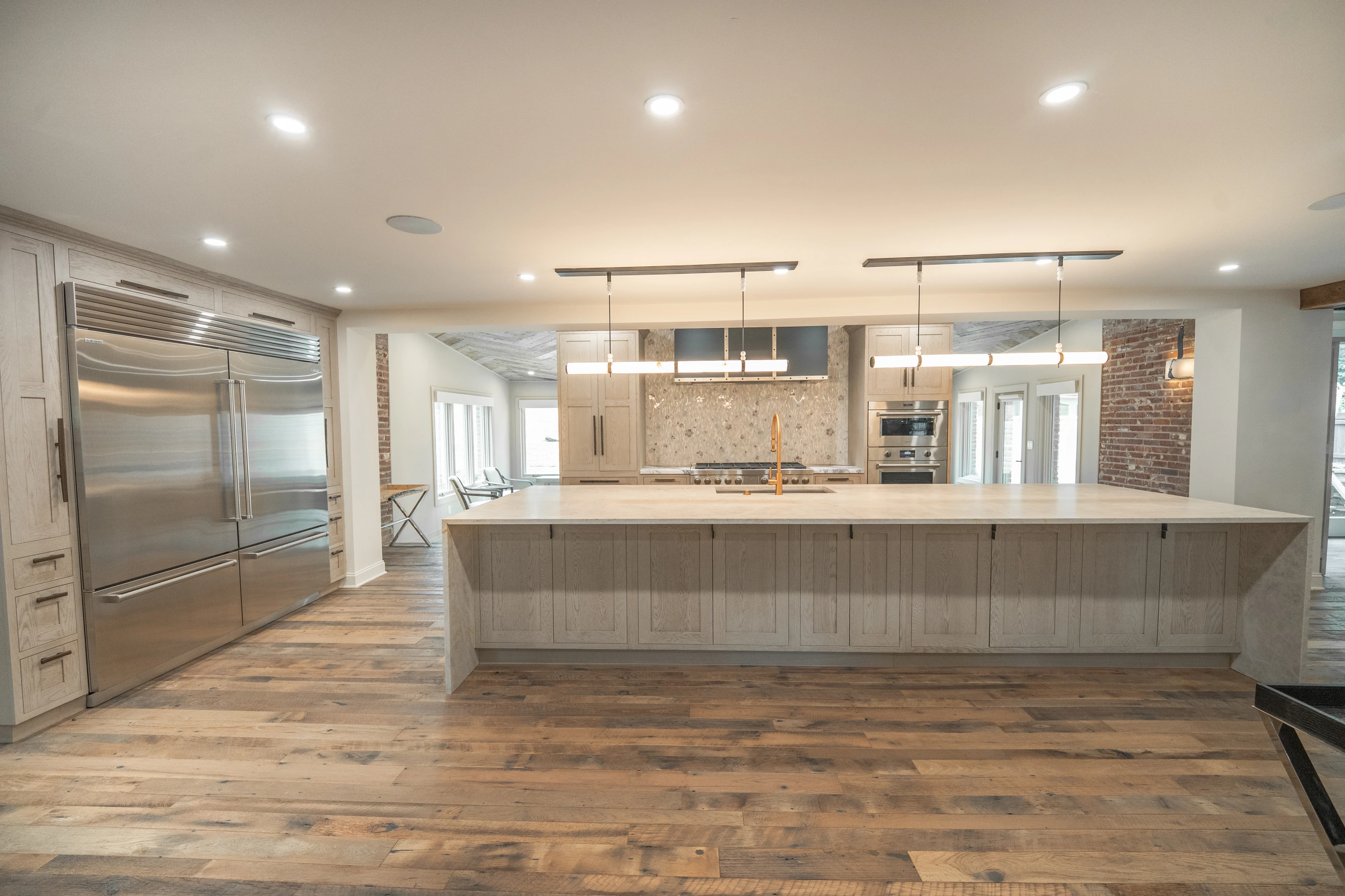 Hart kitchen with pale cabinetry, a large stone-topped island and linear pendant lighting.