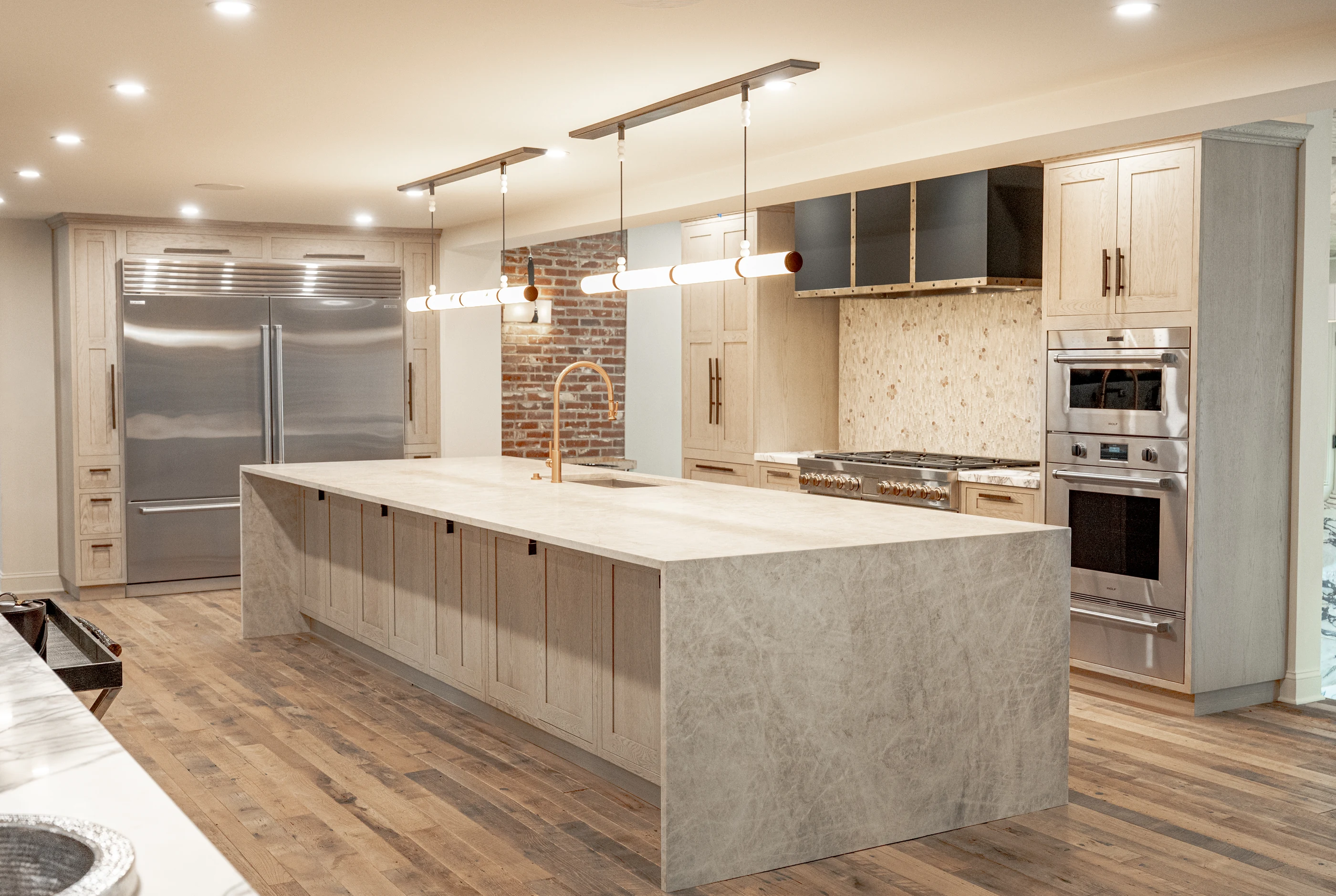 Hart kitchen with a waterfall stone island, pale cabinetry and linear pendant lights.
