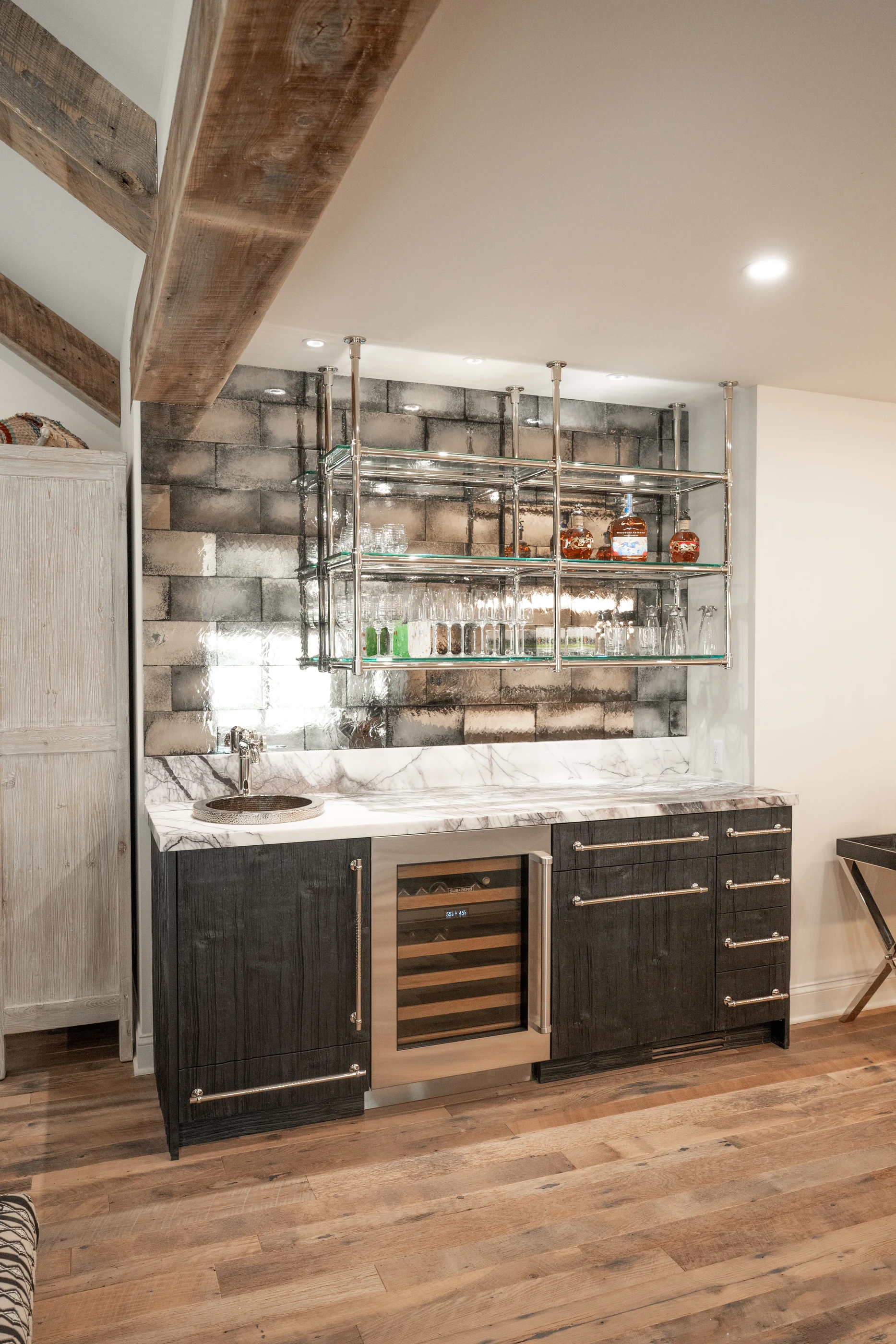 Hart mirrored bar with glass shelves, a stone counter and dark timber cabinetry.