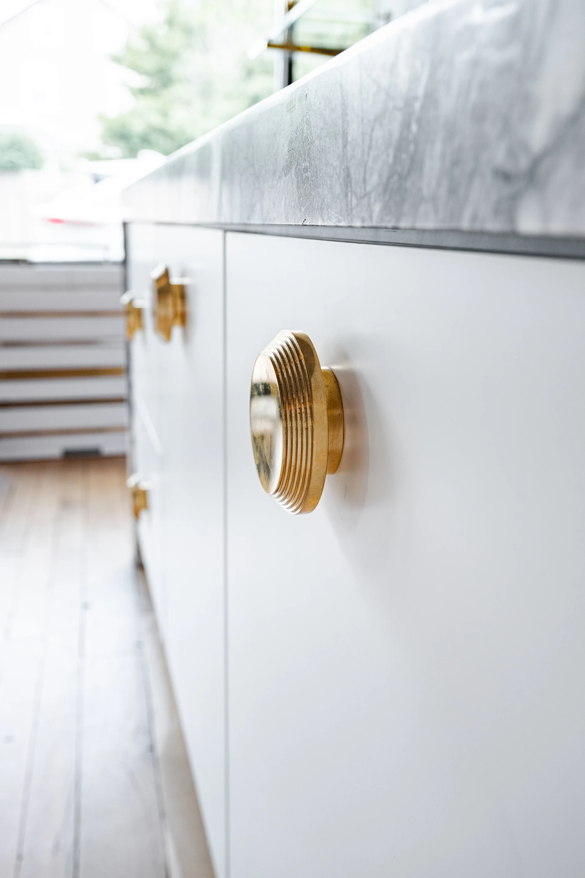 Round brass hardware on pale cabinetry in the Cabinet & Stone Lab showroom.