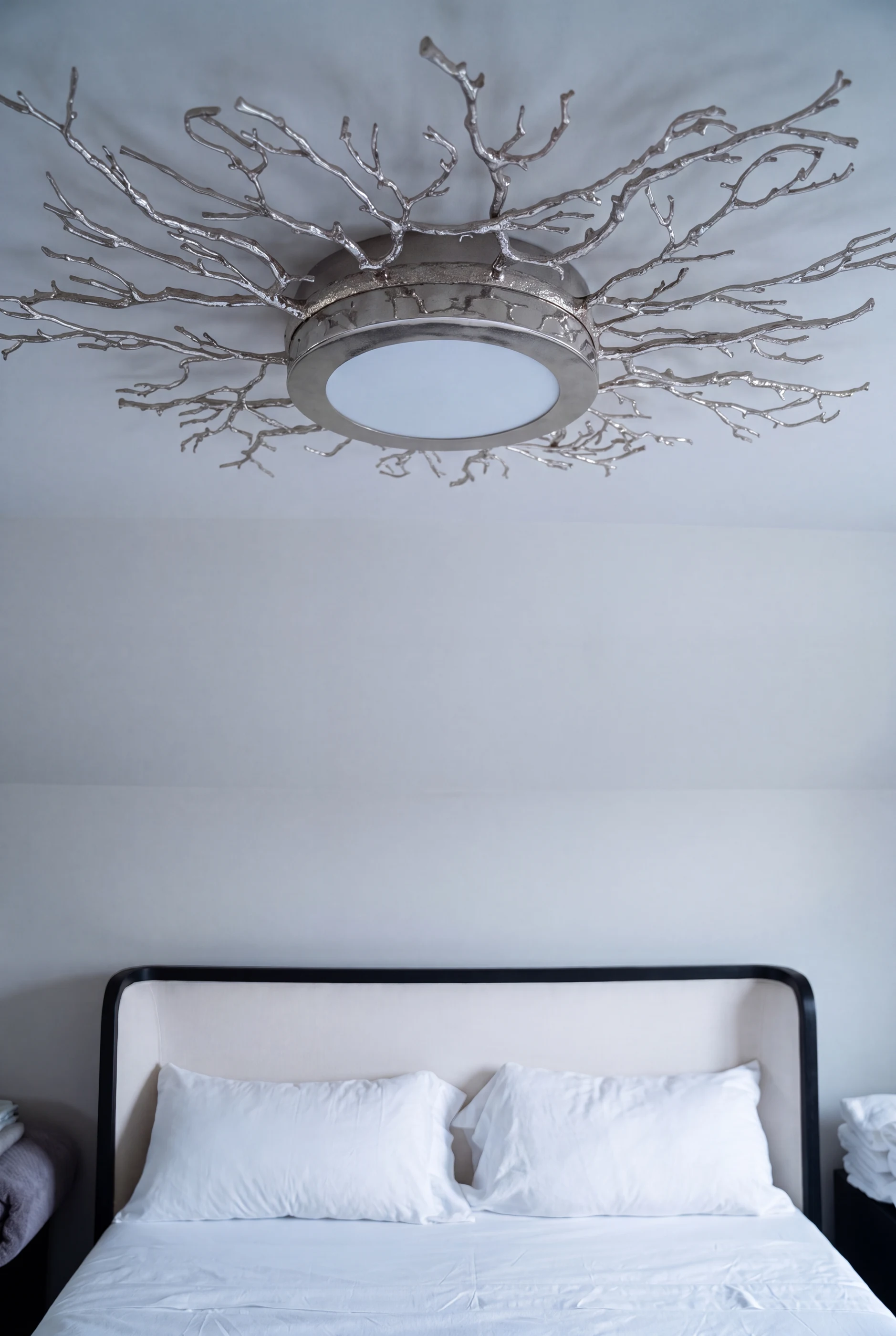 Branch-like ceiling light above a softly upholstered bed at Hart.