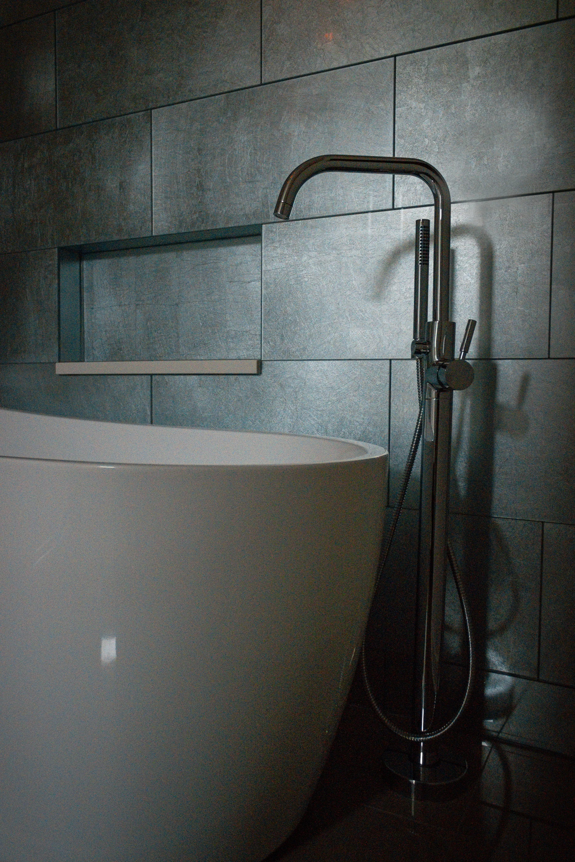 Tub filler and pale freestanding bath against textured tile at Urban Mod.