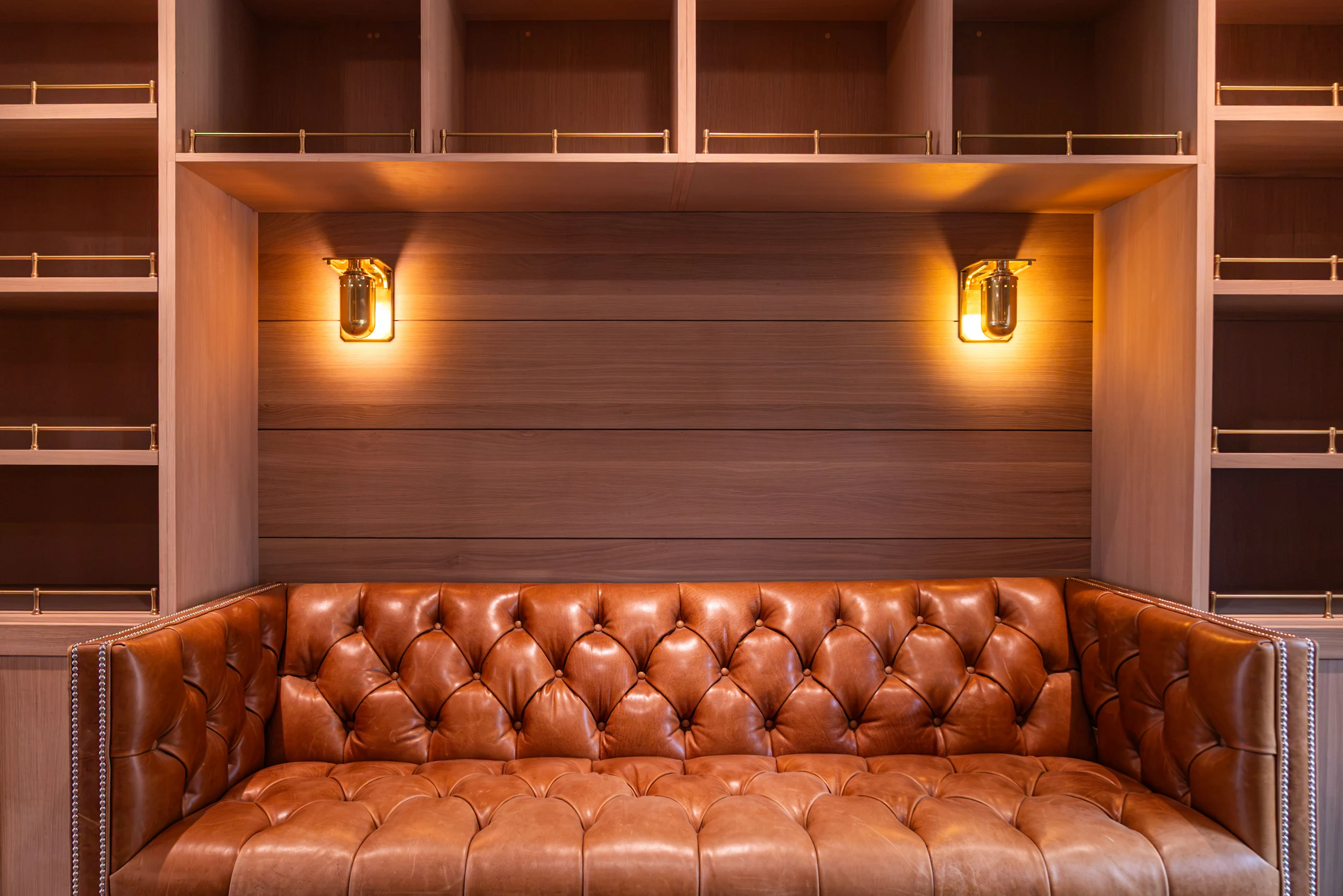 Tufted leather banquette framed by timber shelving and warm brass sconces at Hart.
