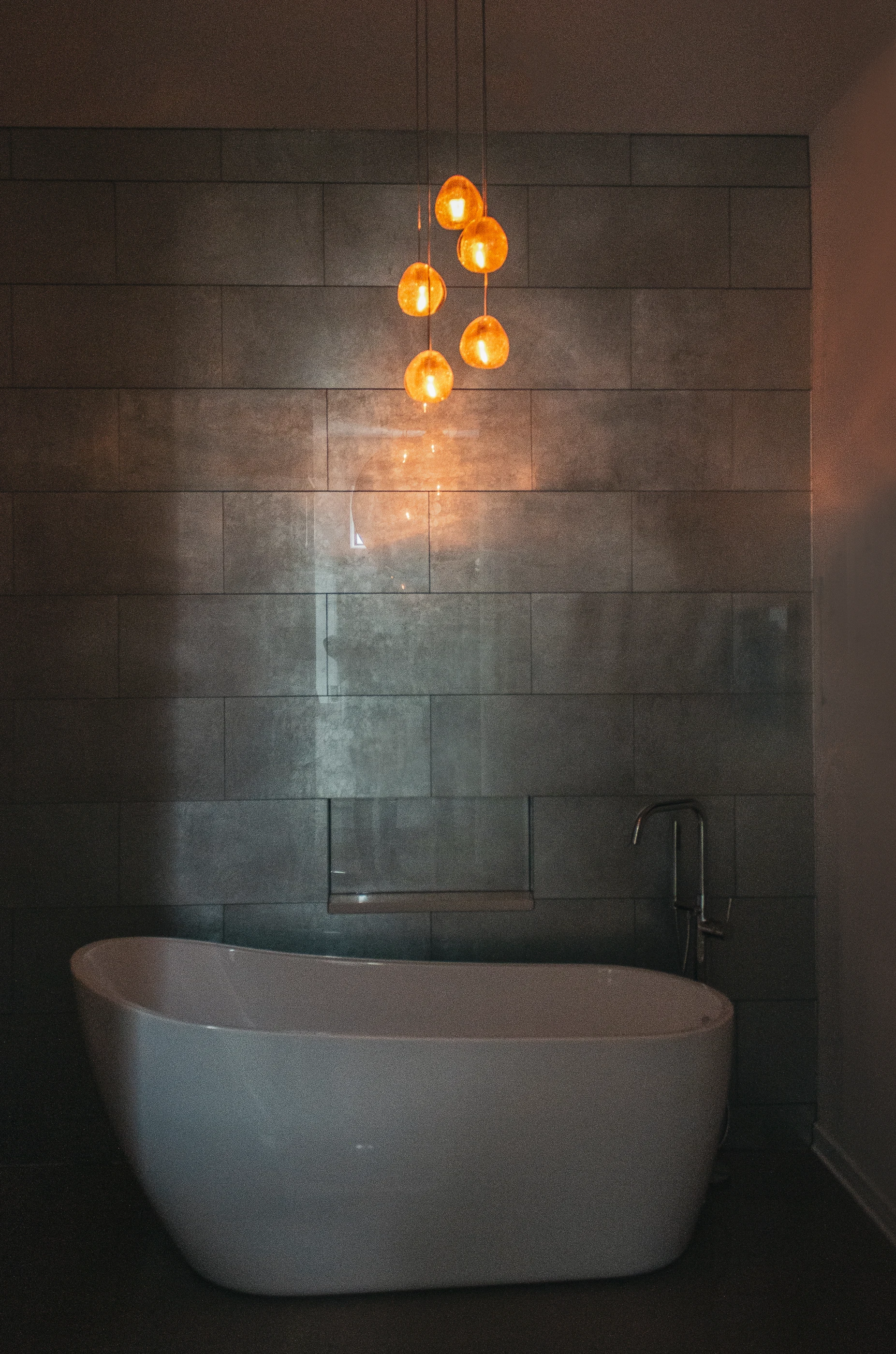 Freestanding bathtub beneath amber pendant lights at Urban Mod.