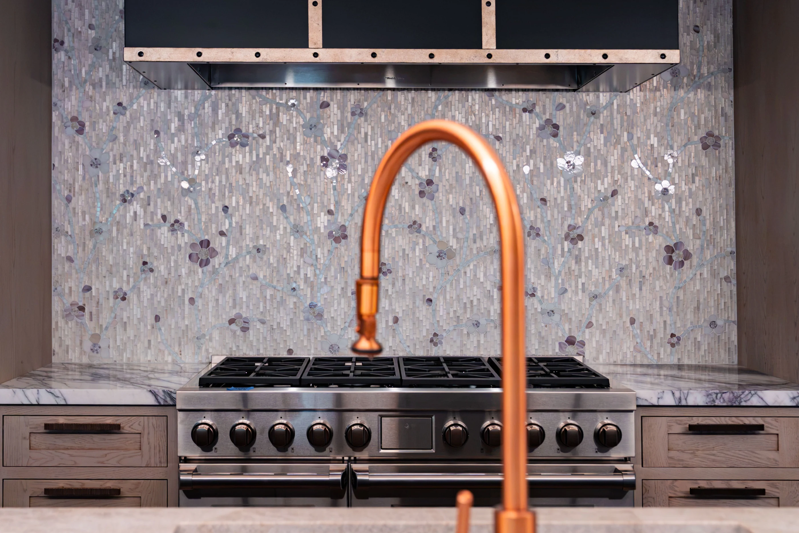Copper kitchen faucet against a detailed mosaic backsplash at Hart.
