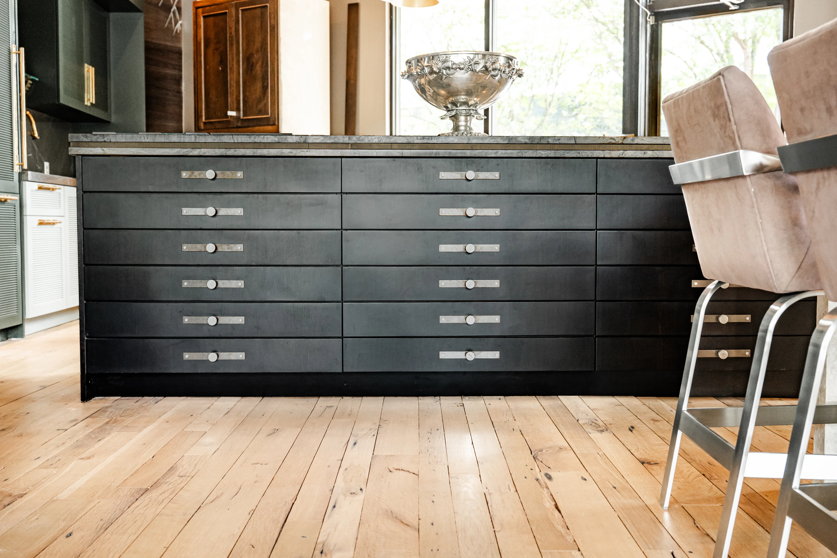 Dark cabinetry with polished pulls and upholstered counter seating in the Cabinet & Stone Lab showroom.
