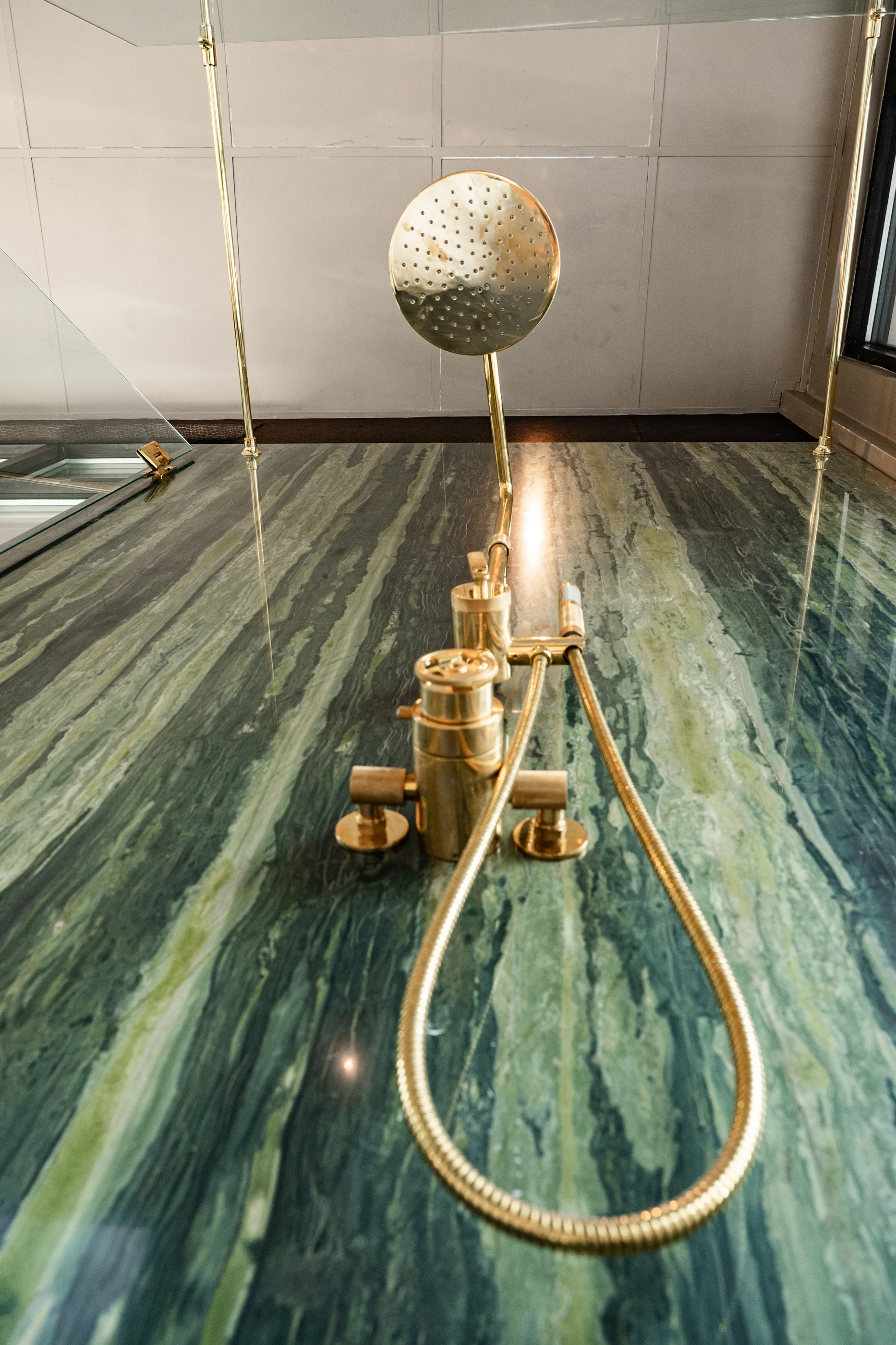 Brass shower fittings against richly veined green stone in the Cabinet & Stone Lab showroom.