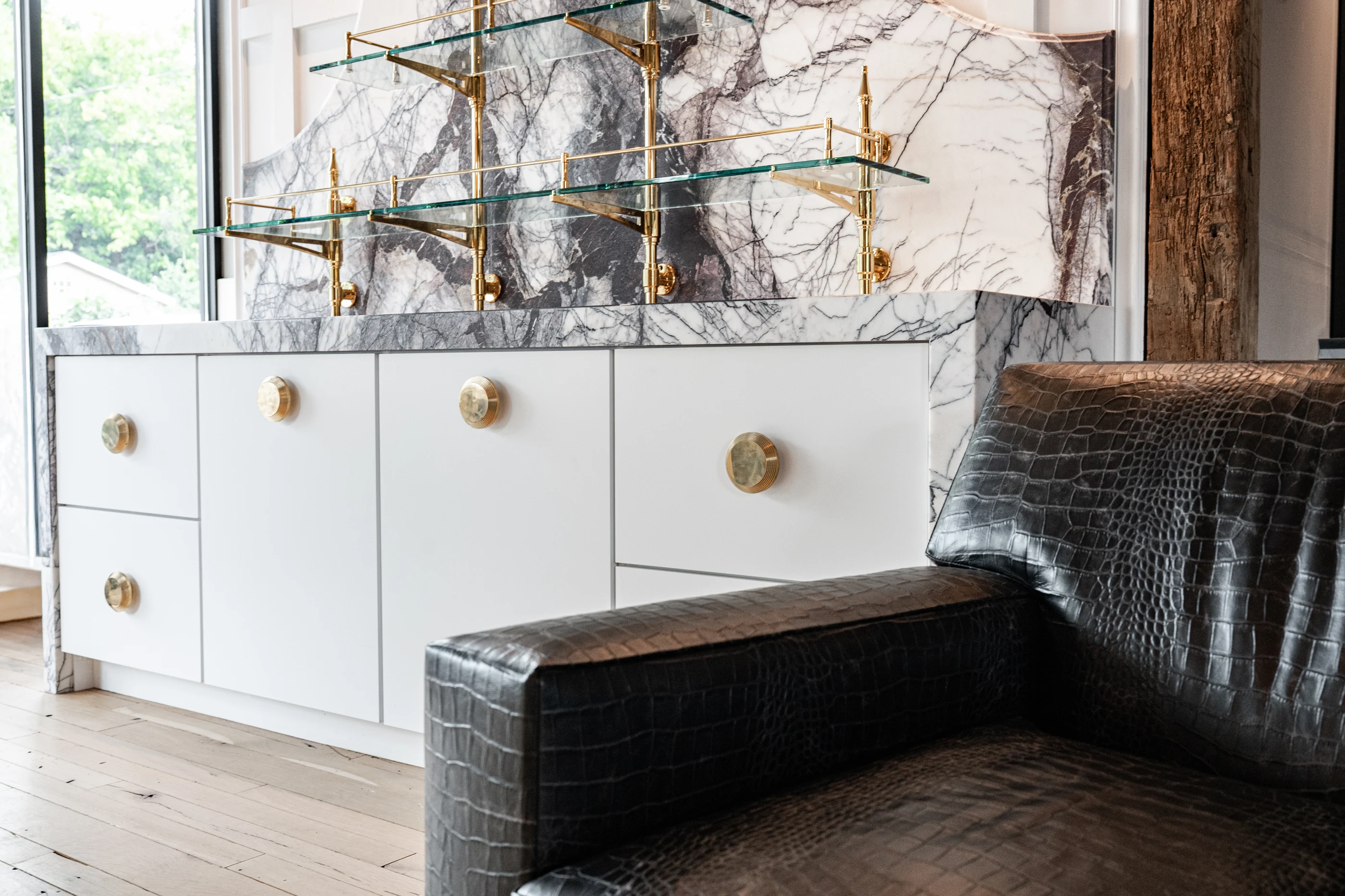 Sculptural stone backsplash, brass shelving and leather seating in the Cabinet & Stone Lab showroom.