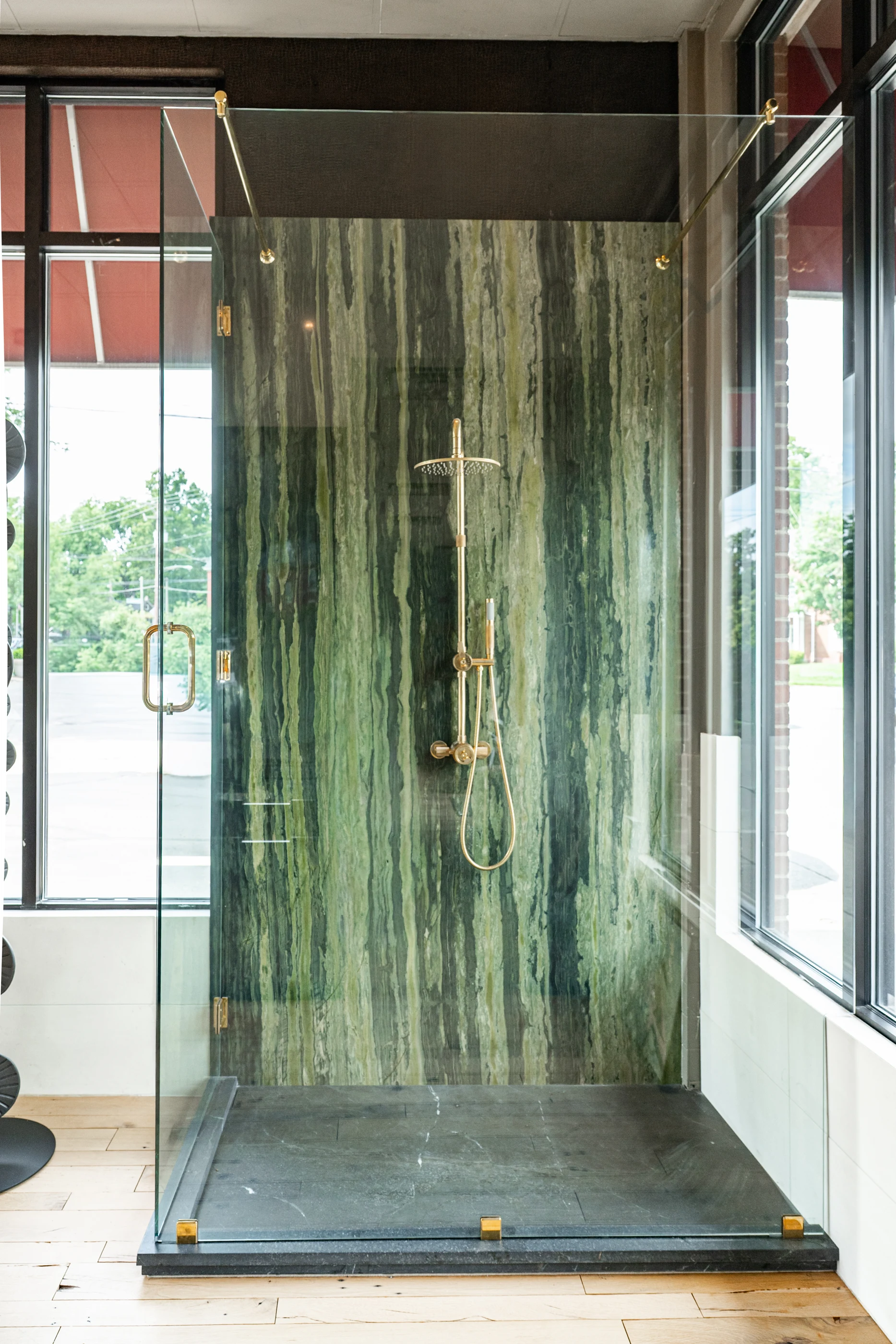 Green stone shower enclosure with brass fittings in the Cabinet & Stone Lab showroom.