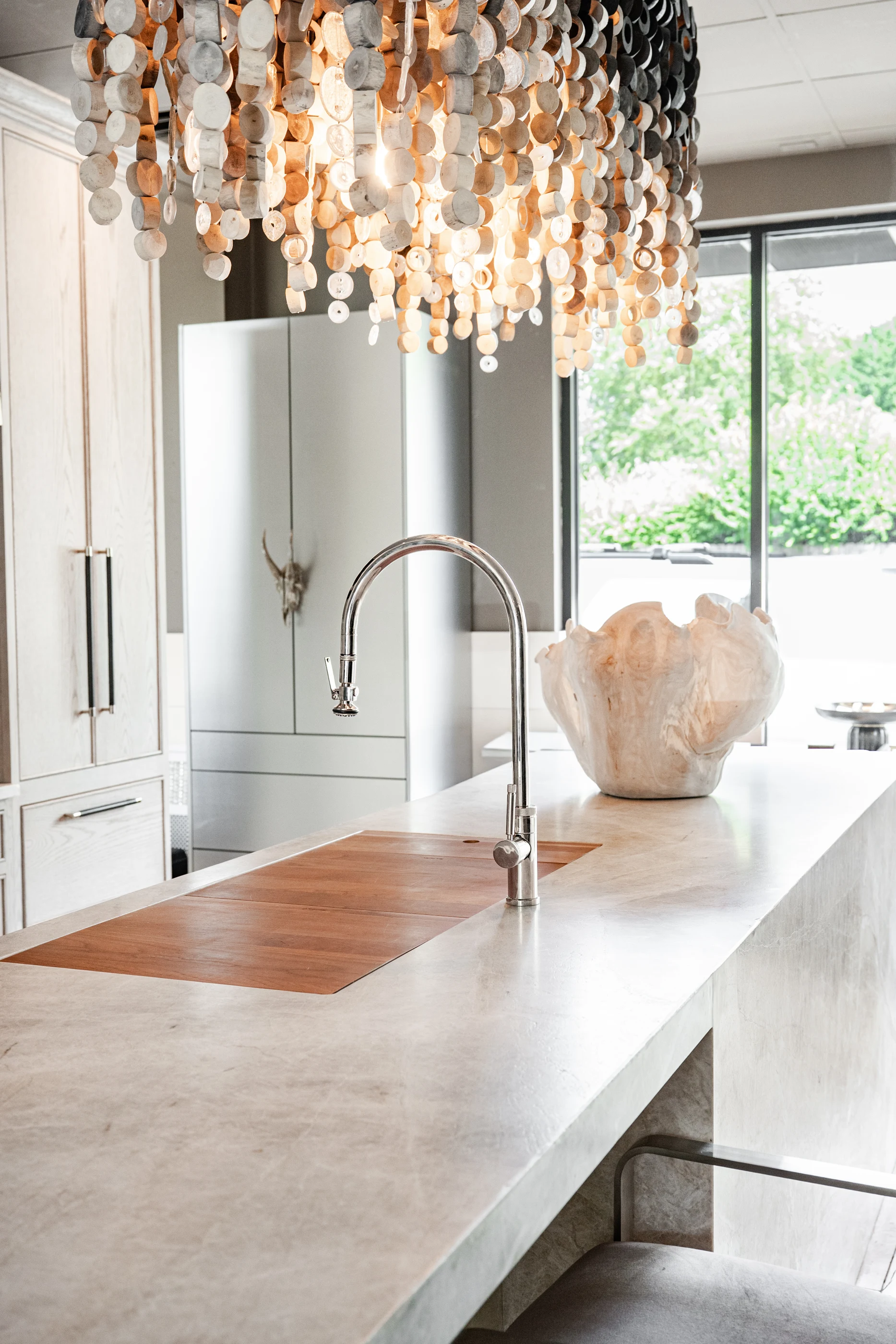 Stone island with a timber insert beneath a luminous disc chandelier in the Cabinet & Stone Lab showroom.