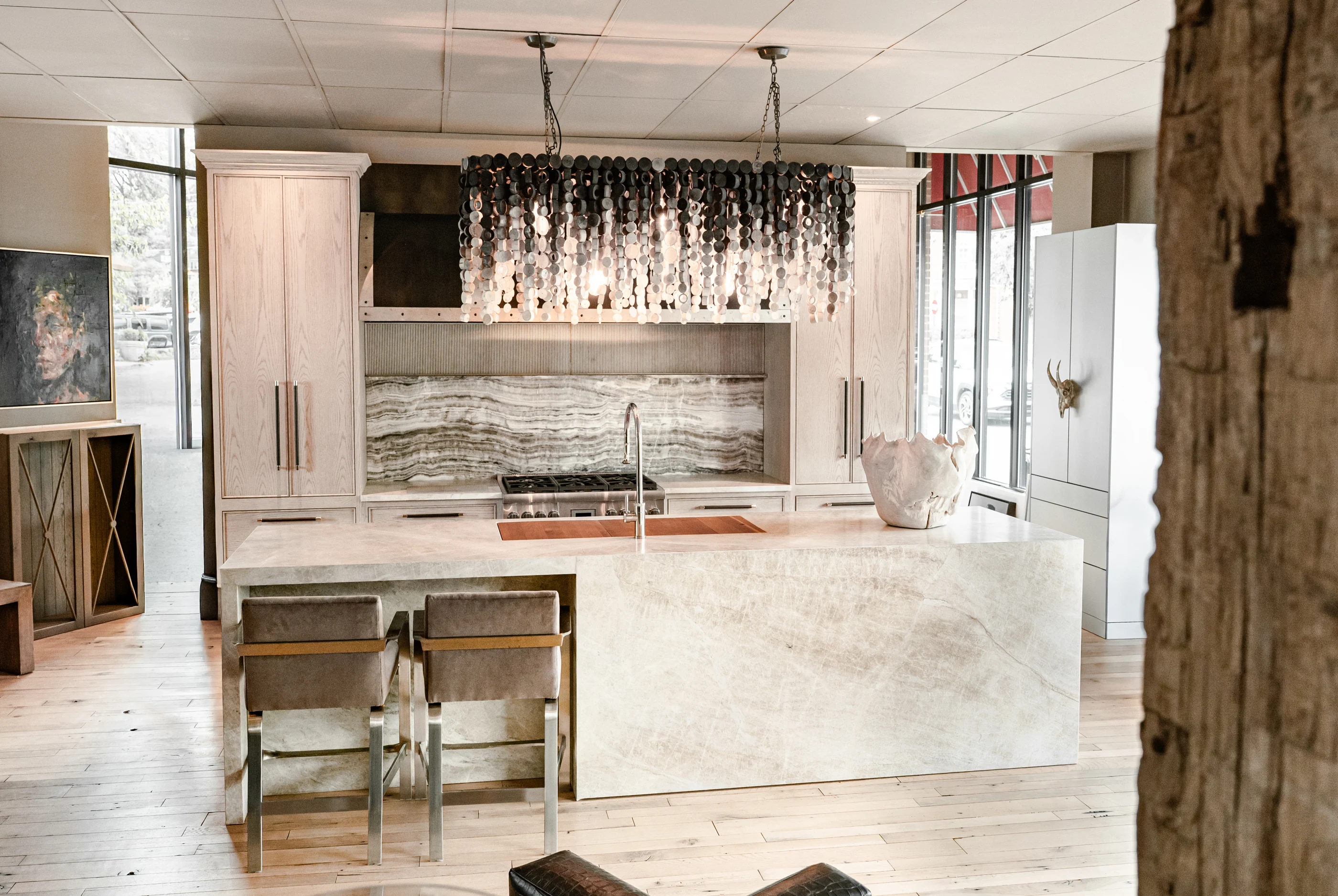 Pale stone island beneath a cascading disc chandelier in the Cabinet & Stone Lab showroom.