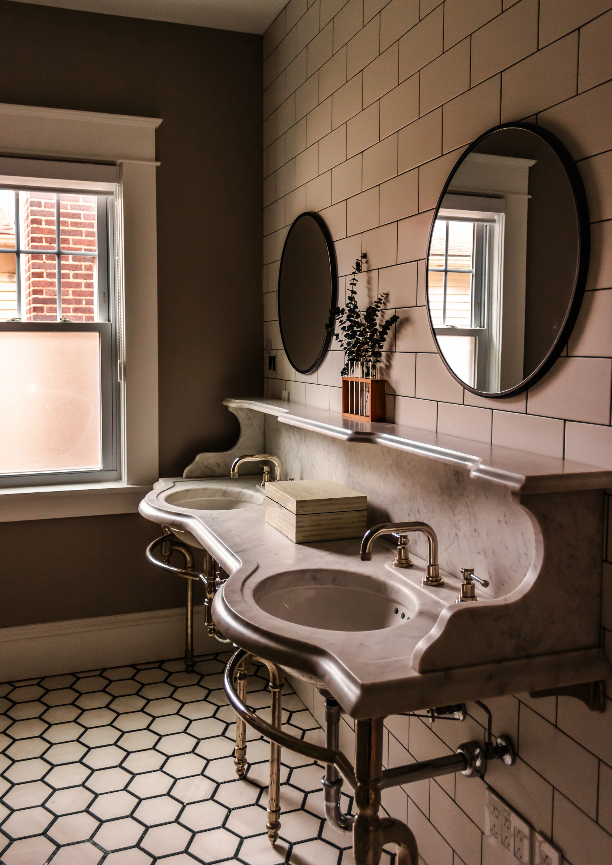 Double stone vanity with oval mirrors and hexagonal floor tile at Chevy Chase.