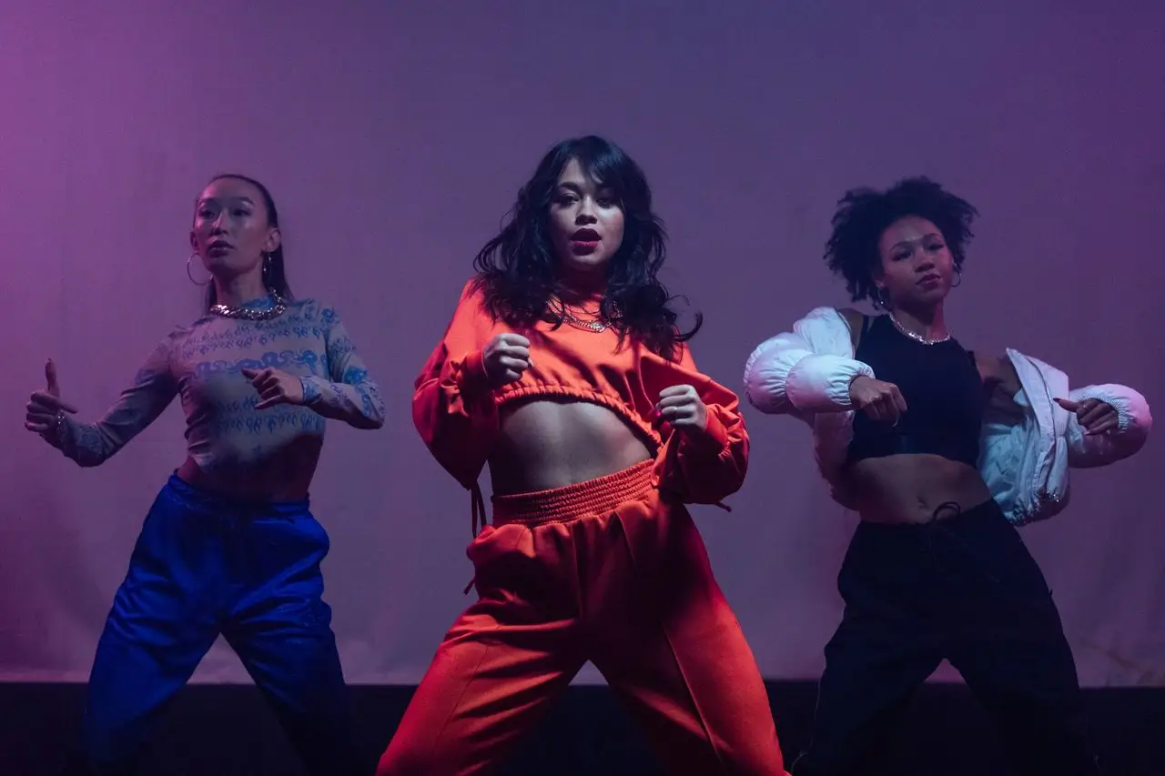 Three women dancing together in a studio wearing casual streetwear.