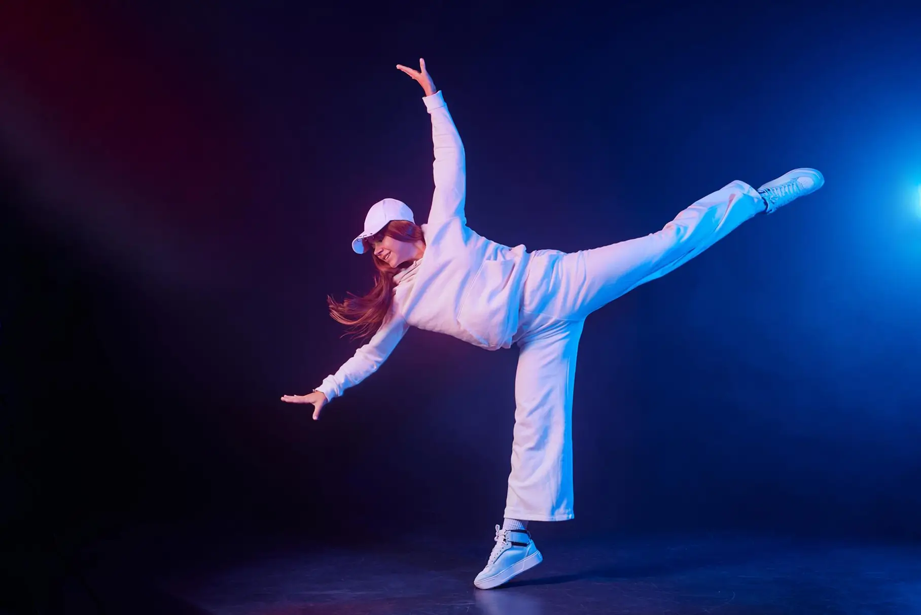 Dancer in white balancing on one leg with arms outstretched under blue light