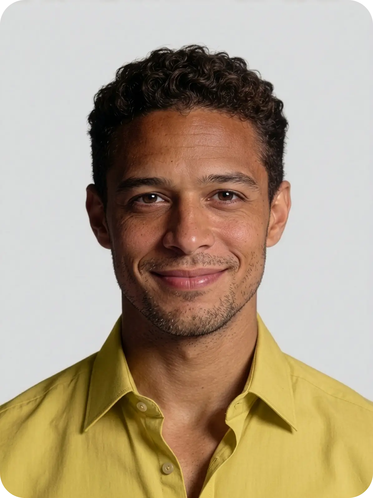 Smiling young man with curly dark hair and light facial stubble wearing a yellow button-up shirt against a plain light background.