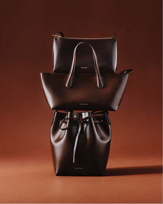 Three dark leather handbags stacked against a terracotta backdrop