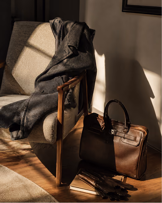 Leather jacket draped over a chair beside a brown leather bag in warm light
