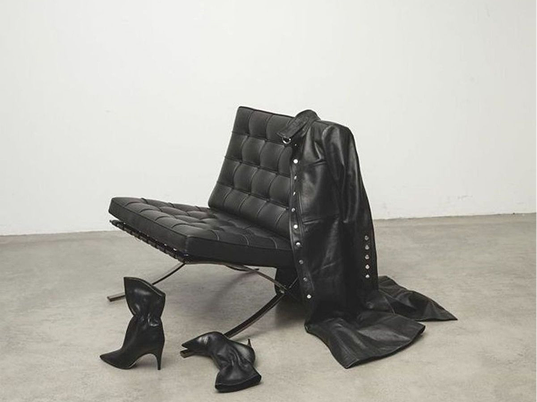 Black leather chair with a jacket, boots and a bag on a grey floor