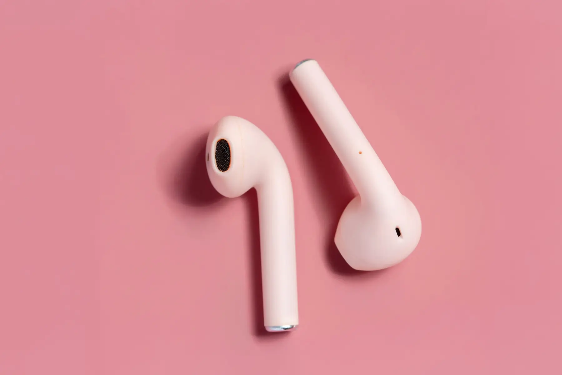 Two pale pink earbuds on a flat pink ground