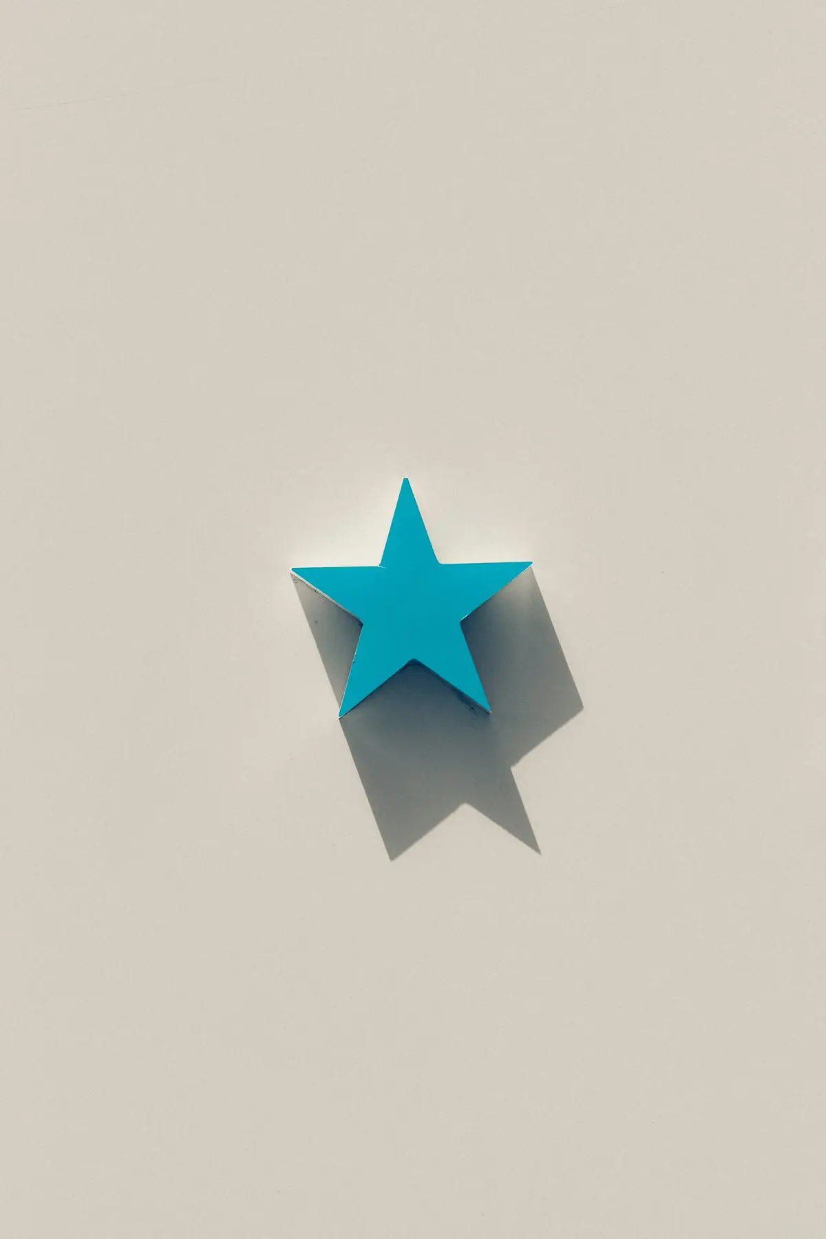 A blue paper star casting a long shadow on a pale ground