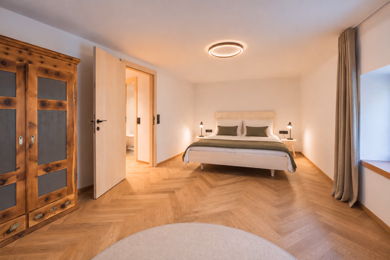 Schlafzimmer im Gregorhof mit Doppelbett, altem Holzschrank und Zugang zum eigenen Bad.