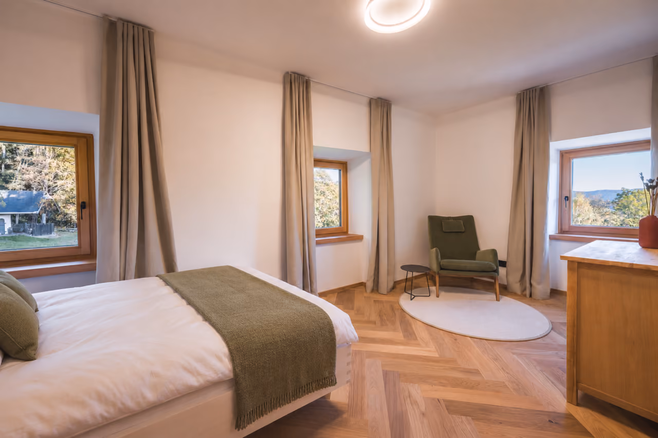 Schlafzimmer im Gregorhof mit Doppelbett, Sessel in der Ecke und Fenstern mit Blick ins Grüne.