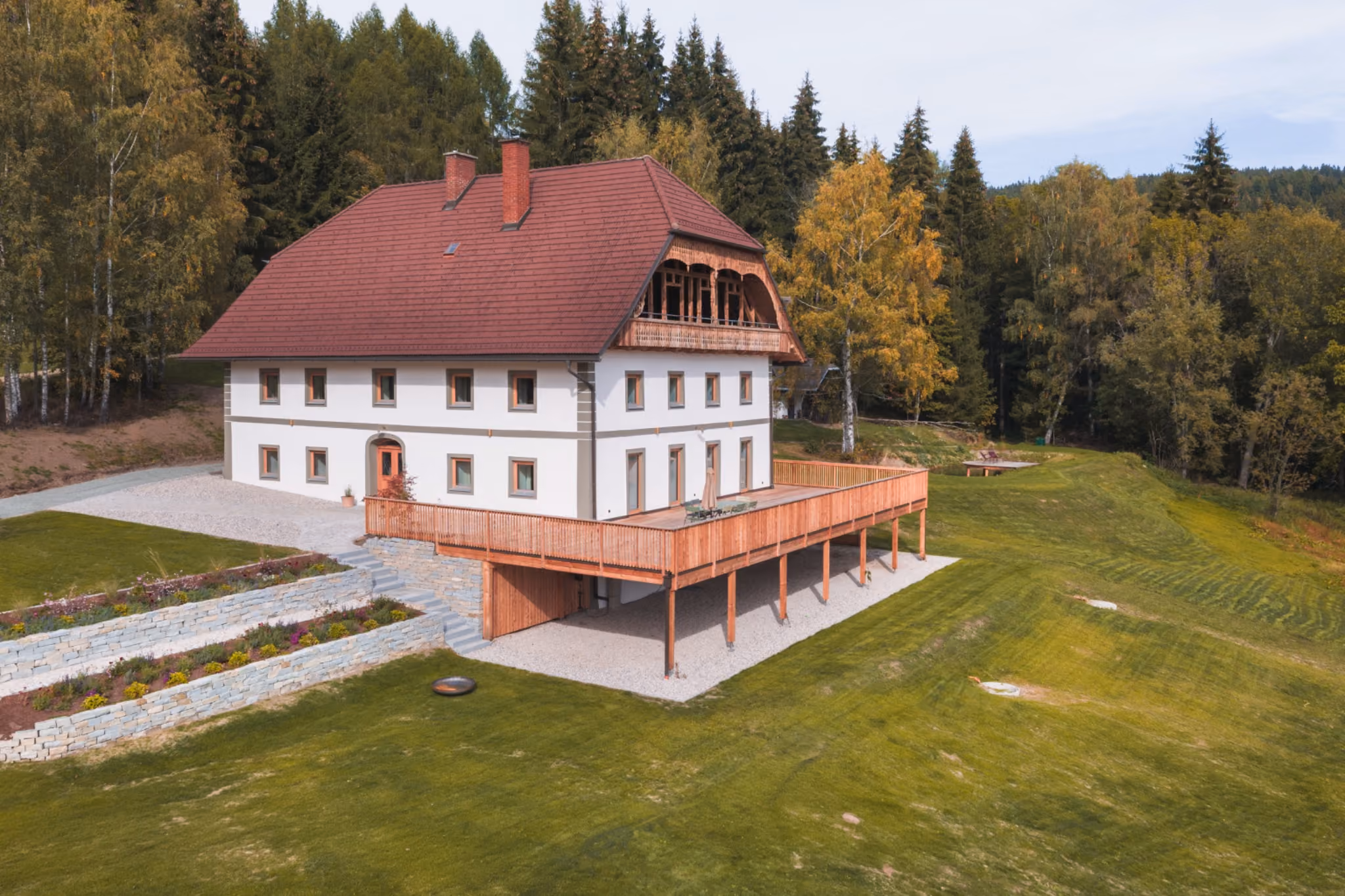 Der Gregorhof mit rotem Dach und großer Holzterrasse, umgeben von Wiesen und herbstlichem Wald.