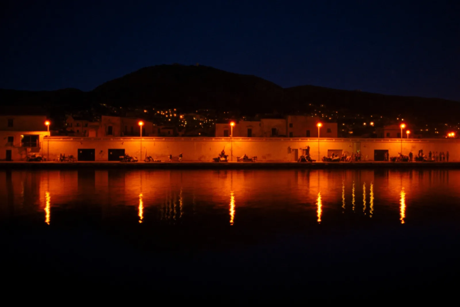 Mediterranean coast at dusk with a single warm orange harbour light in Palermo, Sicily