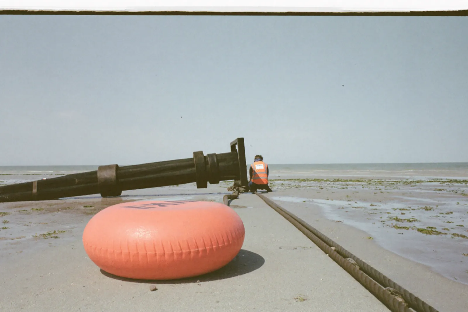 Shore crew in orange high-visibility jackets landing a subsea cable on a wide beach in daylight on the Suffolk coast of