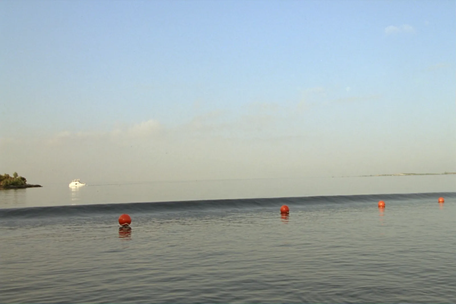 Open sea in daylight, grey-blue swell to a level horizon, one orange buoy or work boat on the water between Crete and