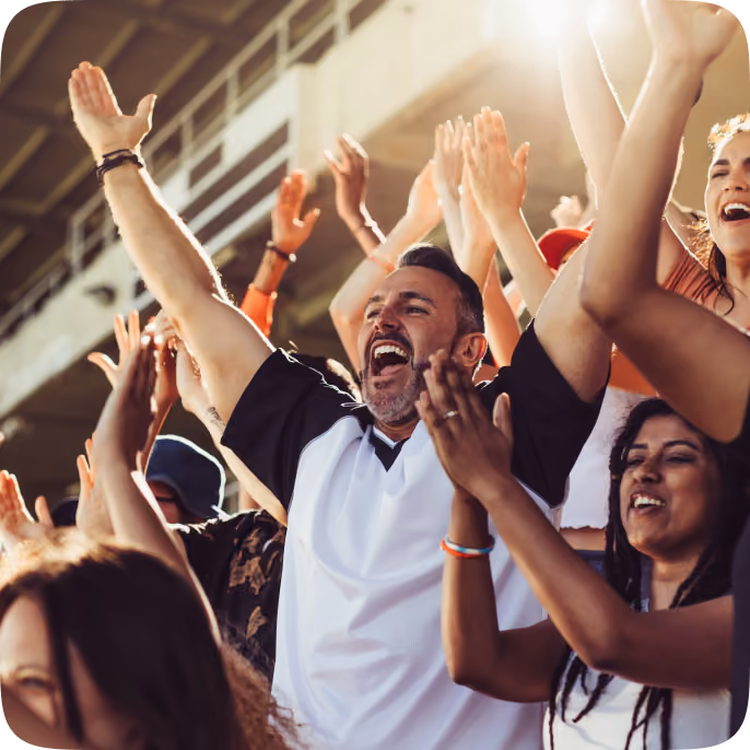 A group of diverse sports fans cheering enthusiastically with raised arms in a stadium, celebrating and clapping.
