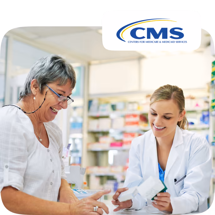A smiling female pharmacist in a white coat shows medication boxes to an older woman with short gray hair and glasses in a pharmacy setting, with the CMS (Centers for Medicare & Medicaid Services) logo above them.