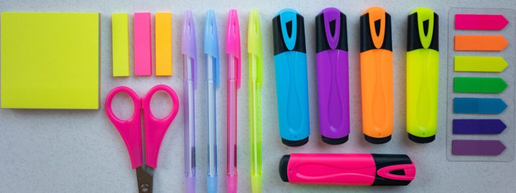 Photo of pens, highlighters, scissors, and Post-Its representing back-to-school shopping for school supplies.