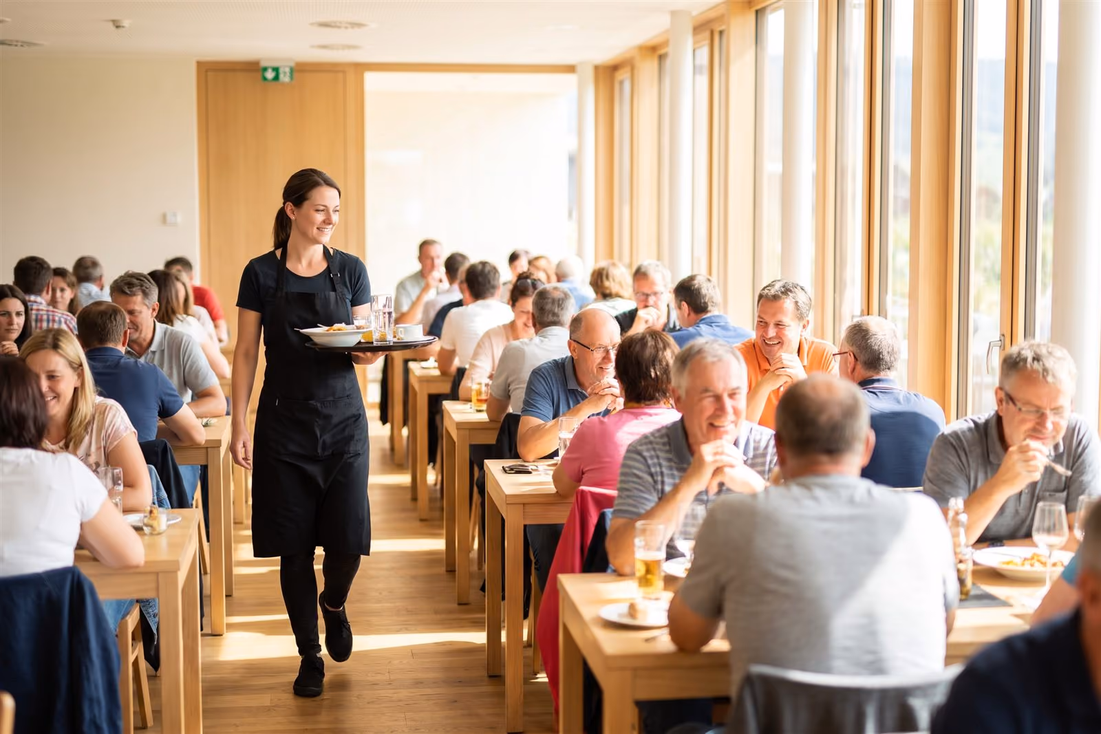 Kelnerka z tacą między zajętymi stolikami w pełnej, jasnej sali restauracji