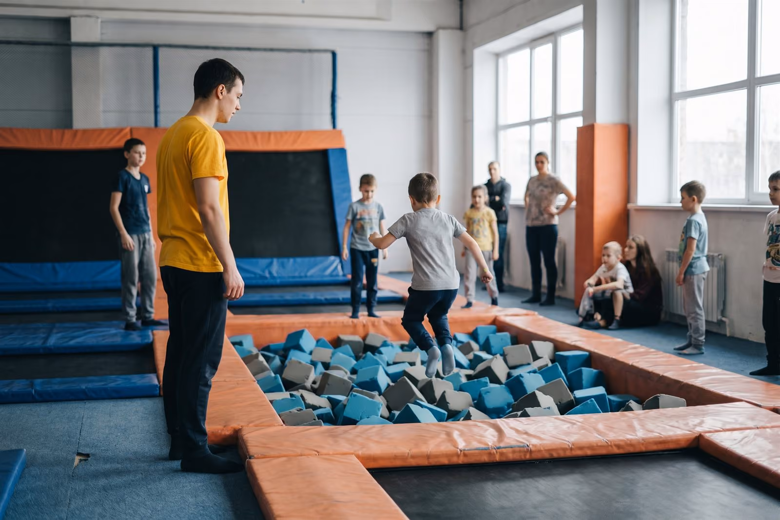 Pracownik obsługi pilnuje strefy trampolin, dzieci skaczą do basenu z gąbek