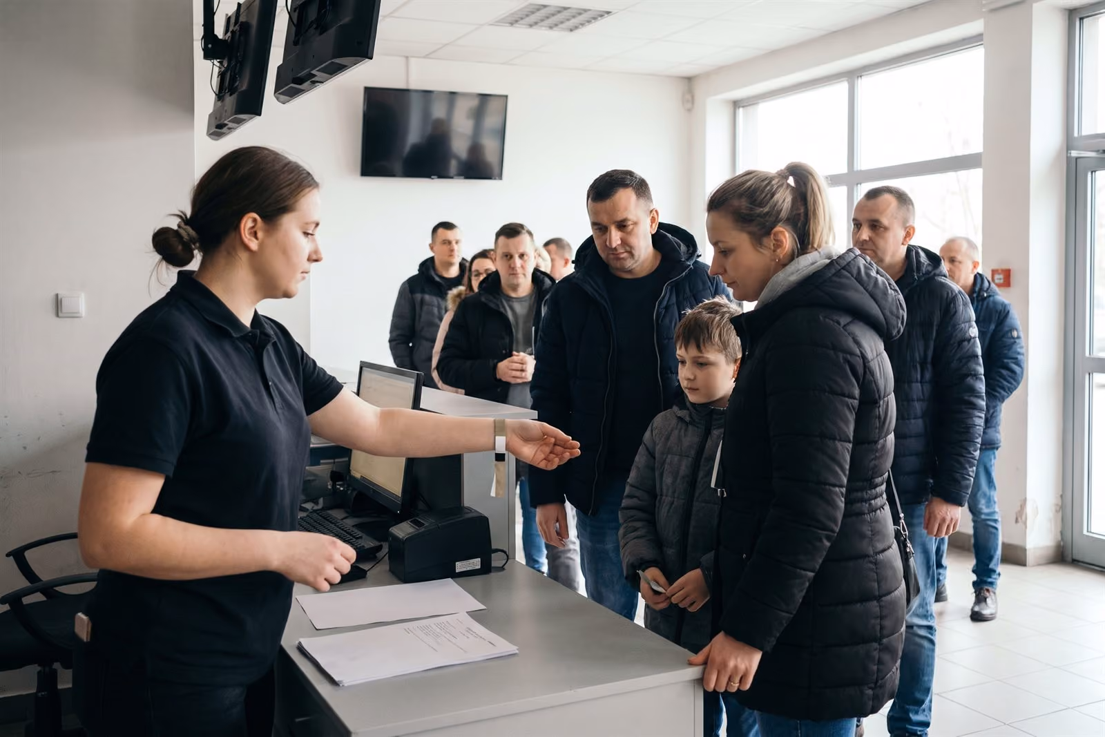 Kasjerka wydaje opaskę rodzinie przy kasie obiektu rozrywkowego, kolejka w tle