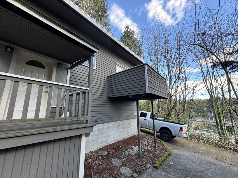 Exterior side view of a two-story dark grey home featuring a newly repaired elevated balcony structure.