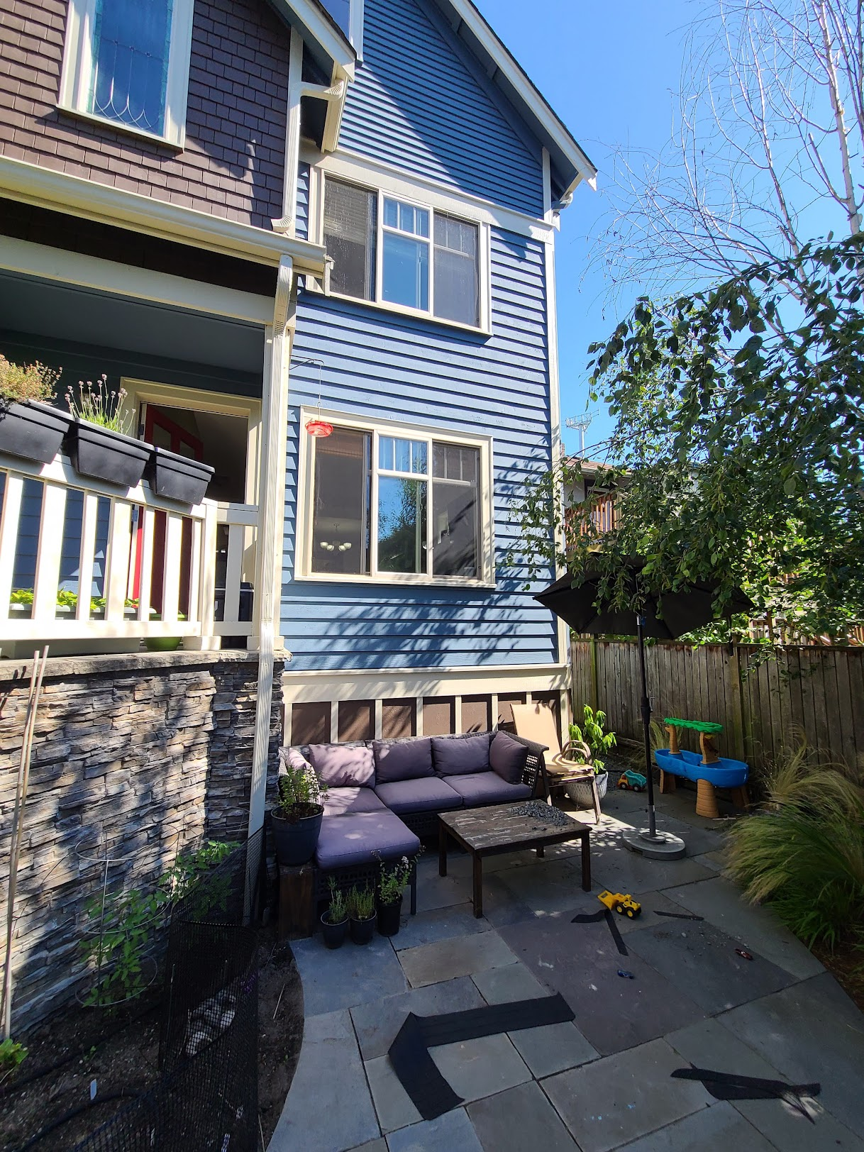 Multi-story blue home featuring a stone patio area with a sectional sofa beneath a balcony.
