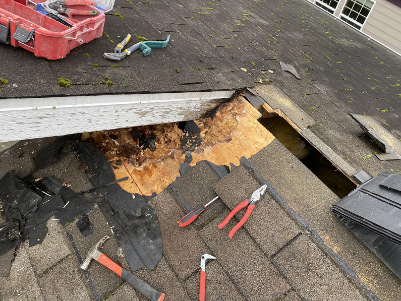 Roof repair in progress showing removed shingles, exposed rotting wood decking, and scattered hand tools.
