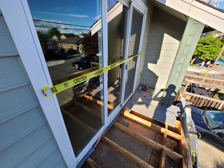 Exposed deck framing and subfloor rot around sliding glass doors marked with caution tape.