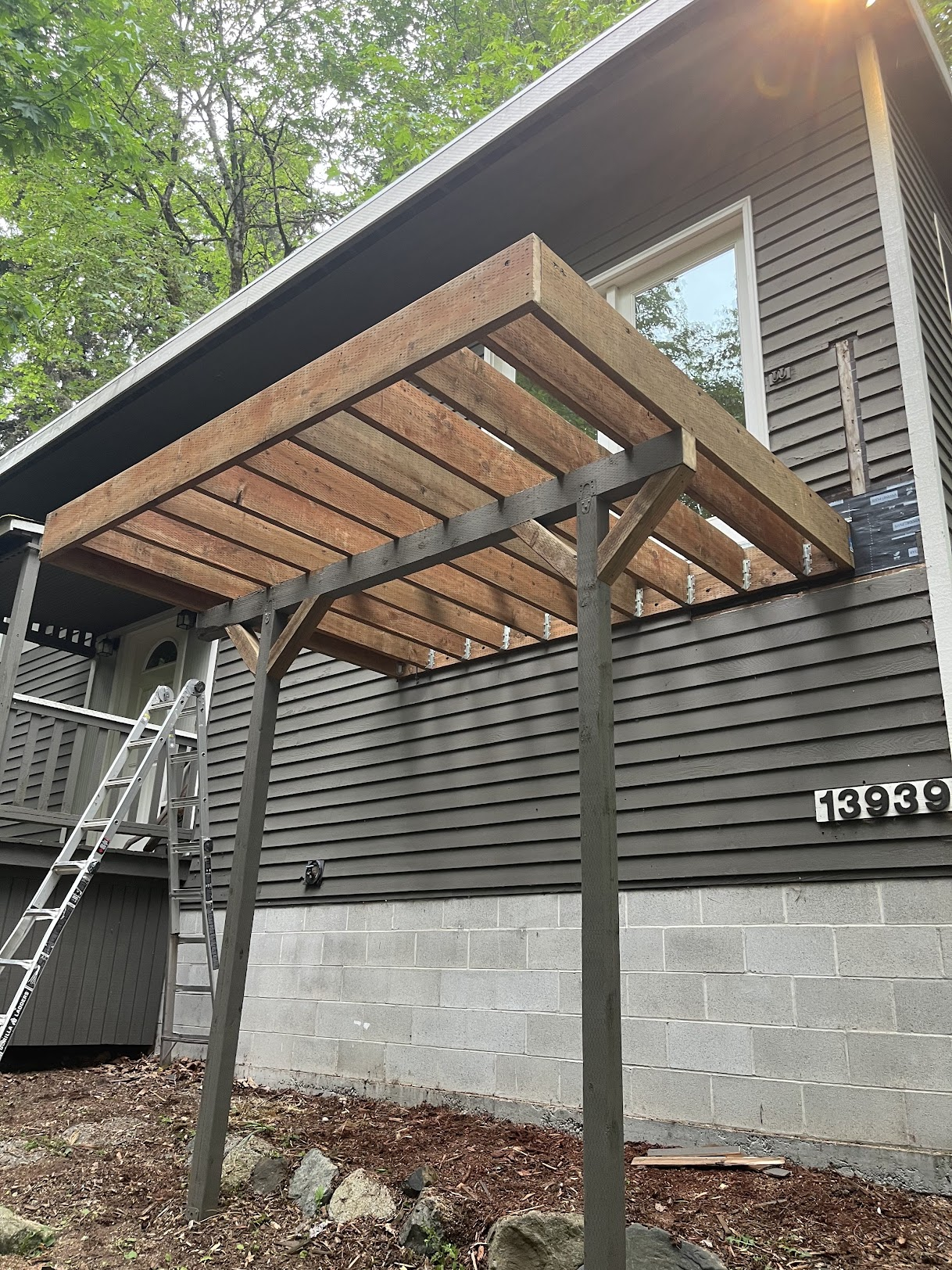 Low-angle view of raw, unfinished wooden deck framing attached to house exterior.
