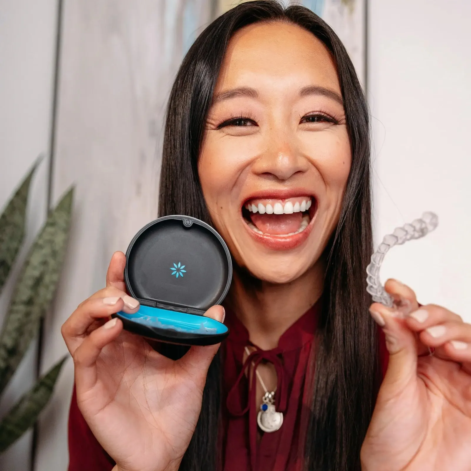 Smiling Invisalign patient holding an aligner case and a clear aligner