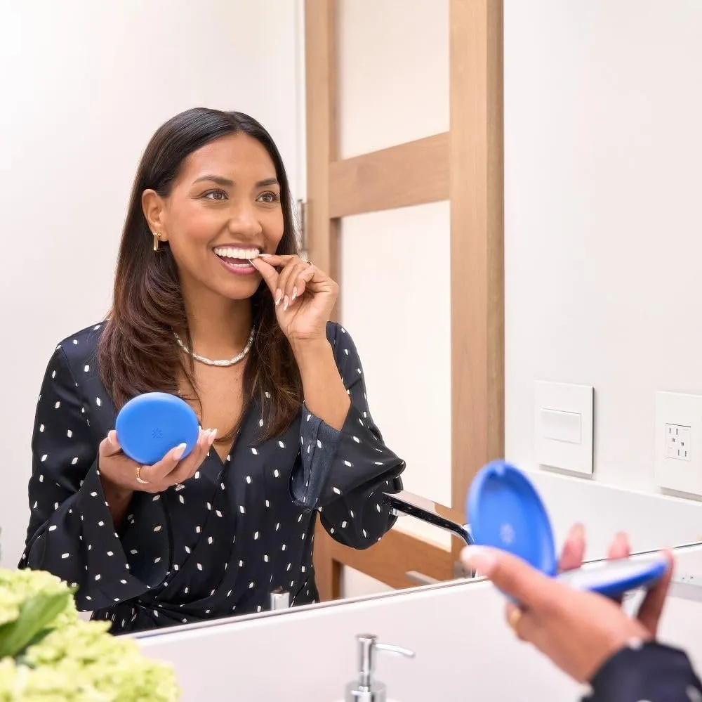Smiling Invisalign patient putting in a clear aligner while holding a blue case