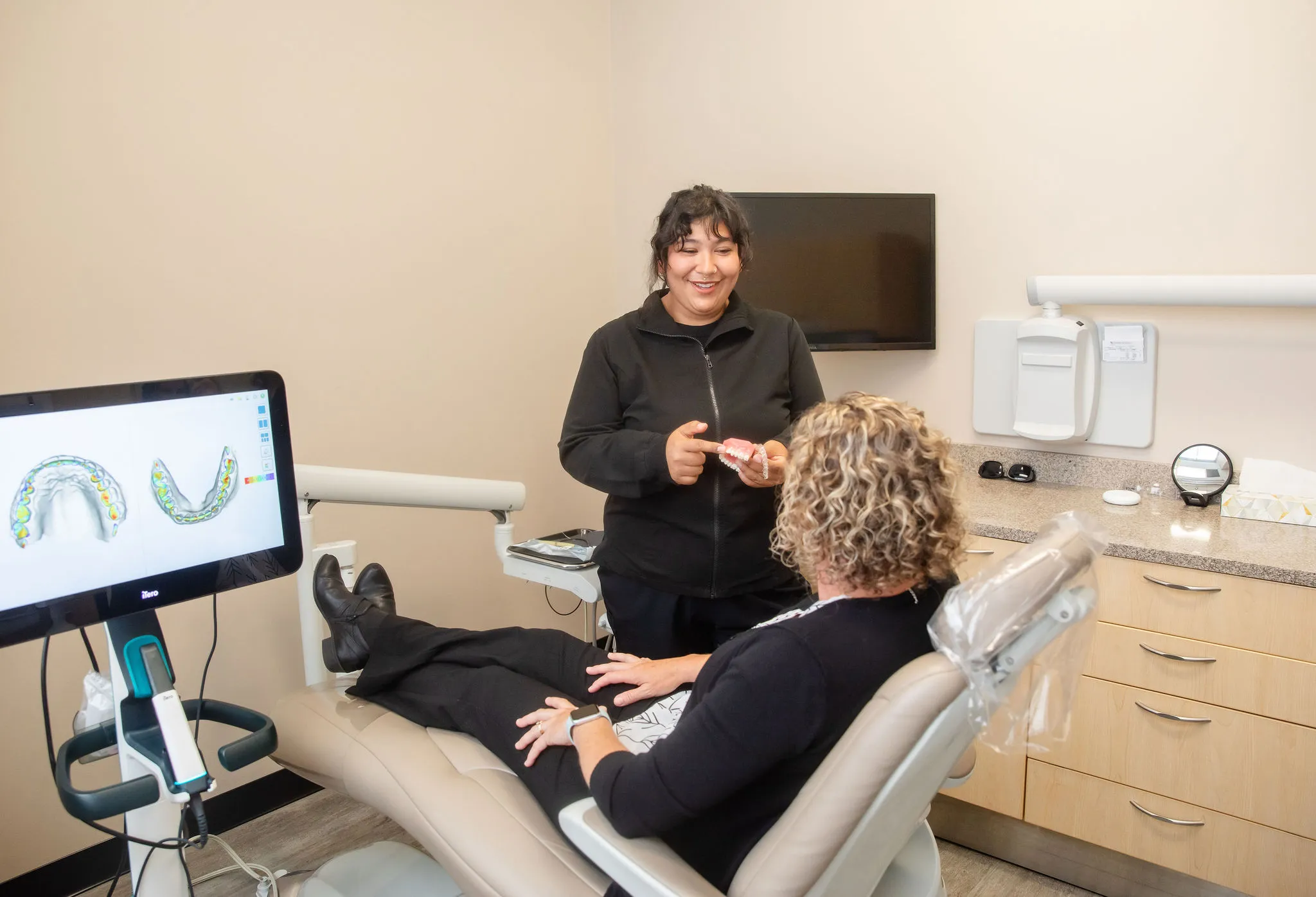 Team member explaining a digital scan and tooth model to a patient in the dental chair.