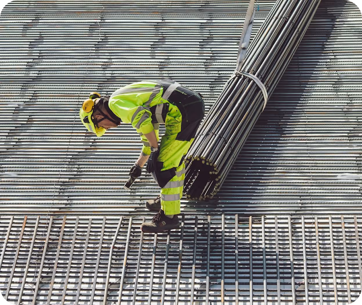 Construction worker in hi-vis gear tying rebar by hand next to a bundle of bars.