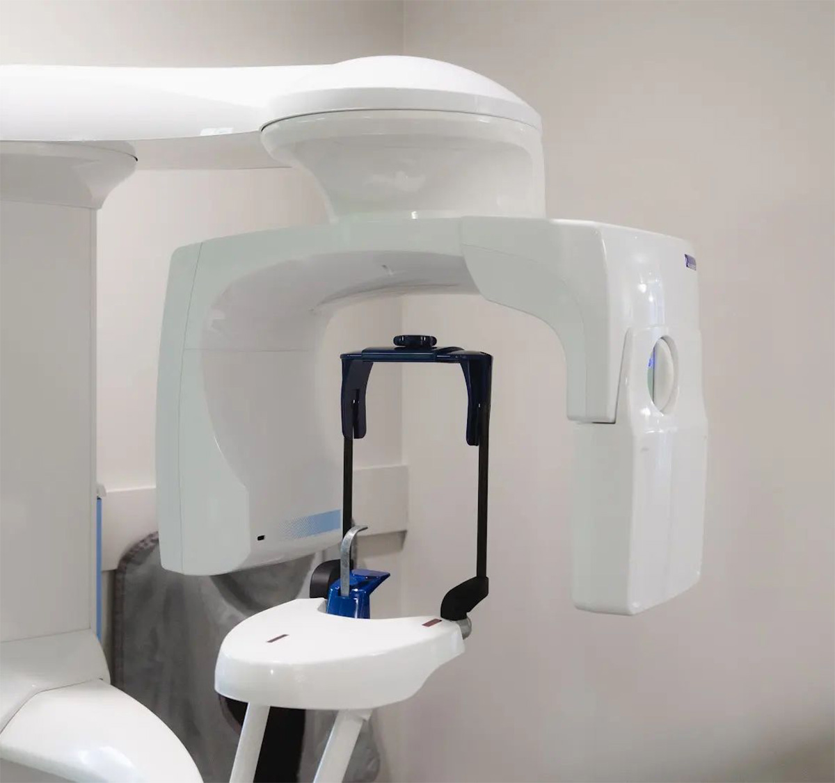 Dental panoramic X-ray machine with patient head positioning components, including a chin rest, forehead support, and side stabilizers in a clinical setting.