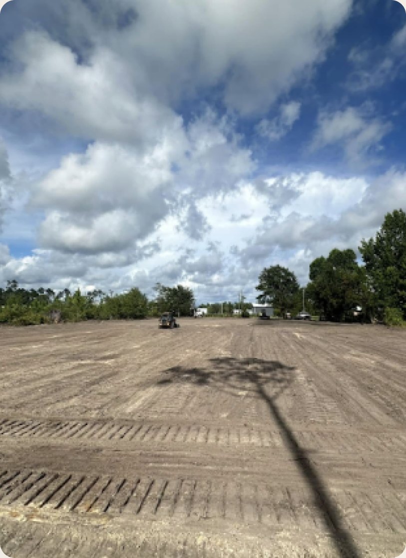 Graded dirt lot with fresh tire tracks under a cloudy sky