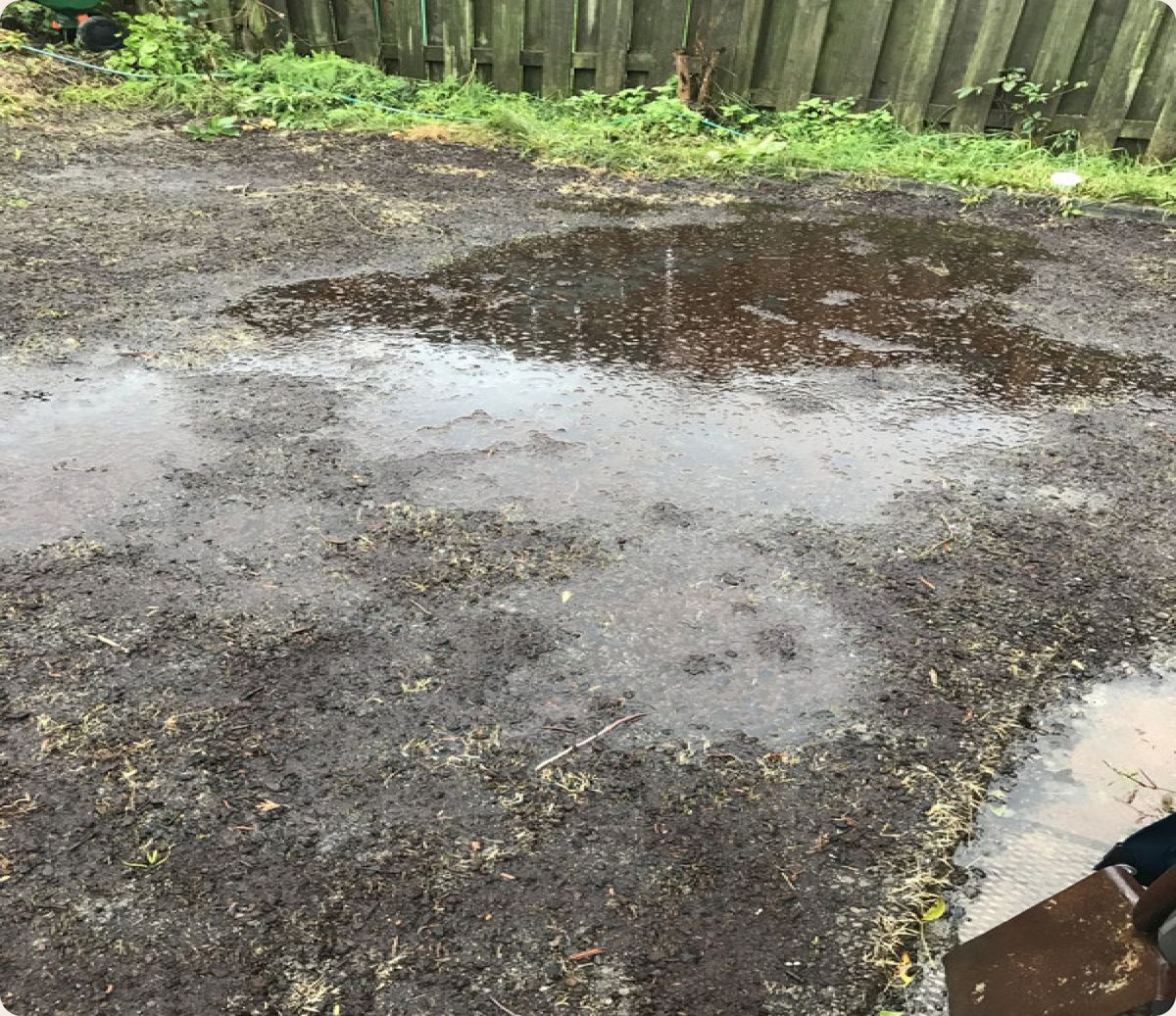 Rainwater standing across bare ground beside a metal fence